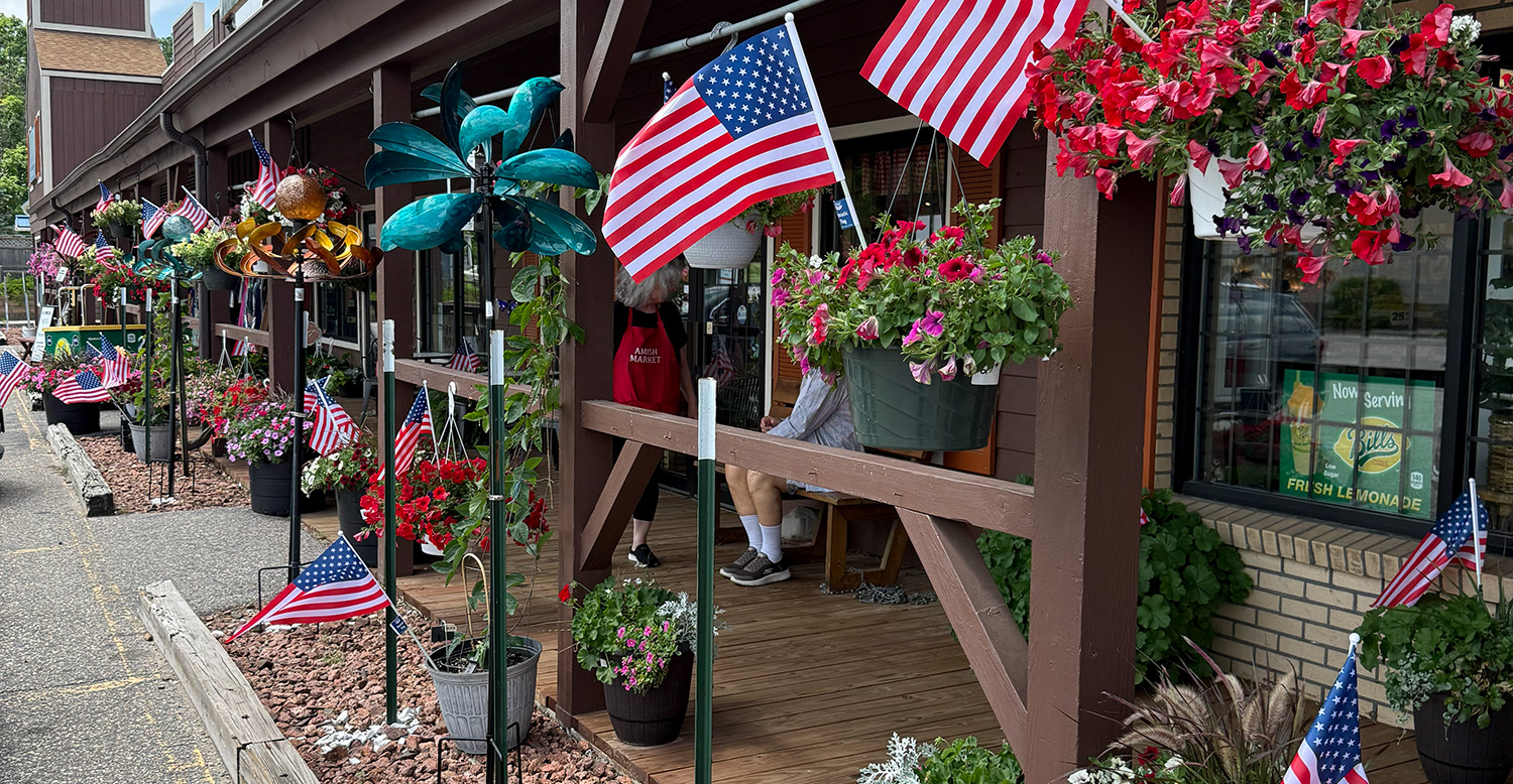 Outside porch in front of the store with hanging baskets of flours, outdoor decorations and American flags